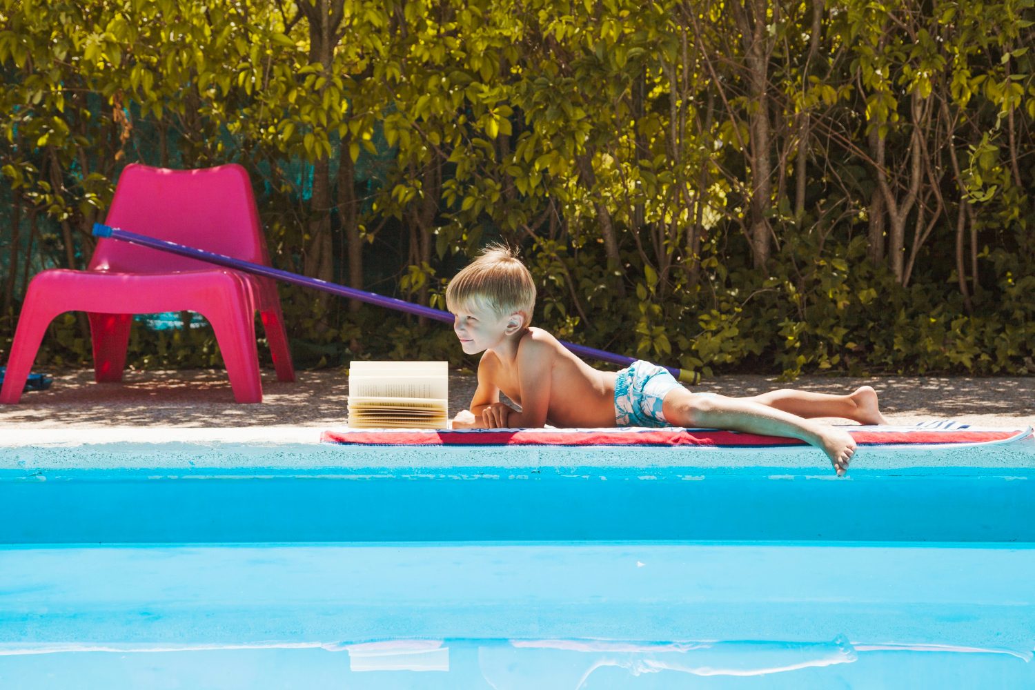 como limpar piscina de plástico: criança na beira da piscina lendo livro